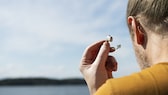 Mann mit einem Hörgerät in der Hand am Strand