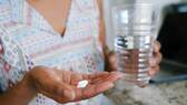 Zwei Ibu Tabletten in der Hand mit einem Glas Wasser