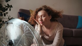 Frau sitzt vor dem Ventilator und lässt sich abkühlen.