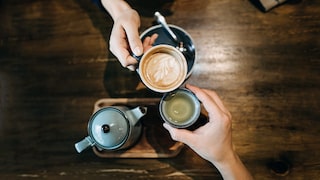 Zwei Personen stoßen mit Kaffee und Tee an.