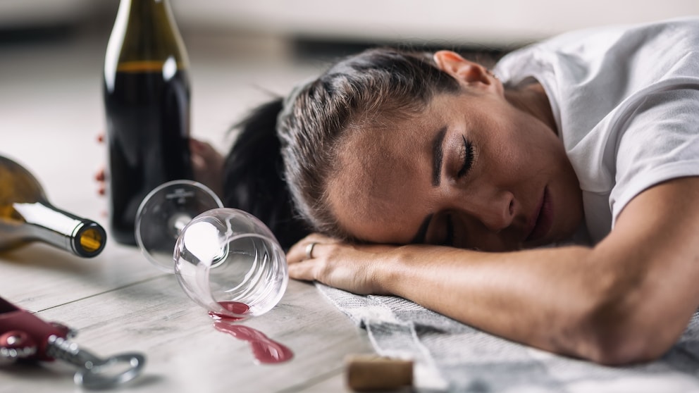 Drunk woman fell asleep on the floor at home with glass of red wine spilled next to her.