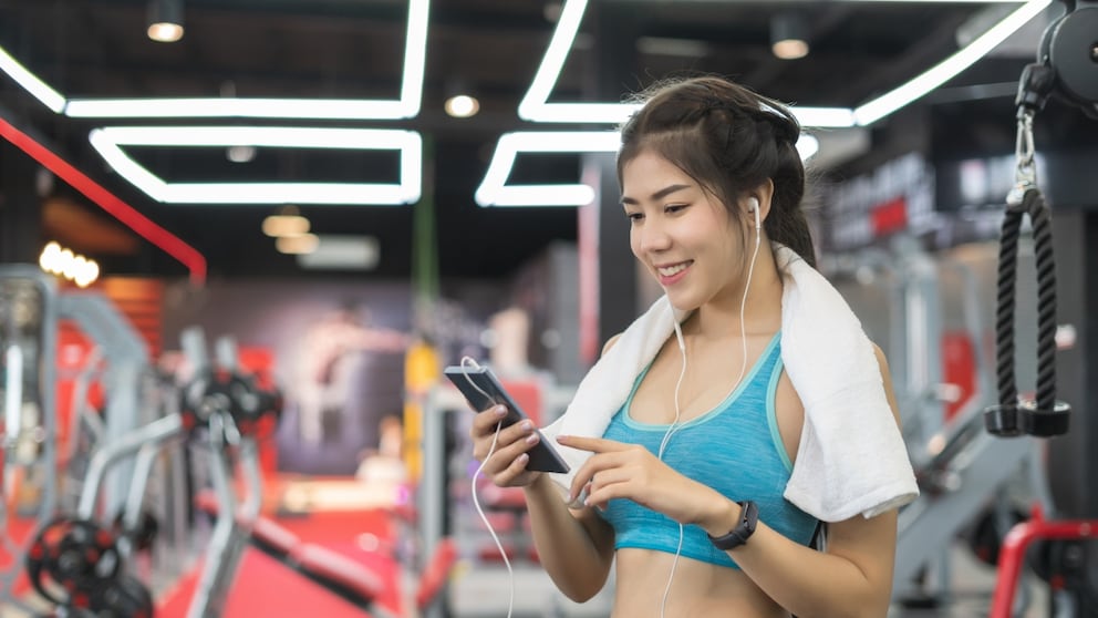 Frau im Fitness-Studio mit Handtuch und Smartphone