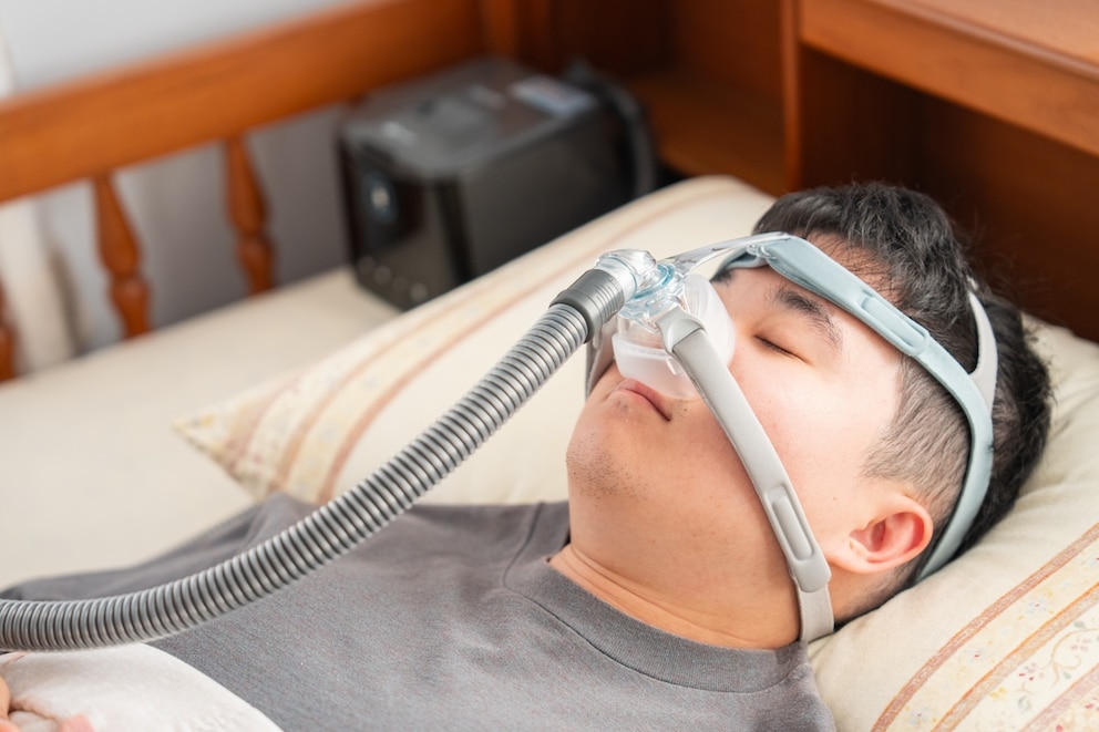 Mann trägt bei hohen Temperaturen Schlafmaske zur Behandlung seiner Schlafapnoe