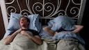 Pille gegen Schlafapnoe? Ein Mann liegt schnarchend neben einer Frau im Bett, die sich ein Kissen &uuml;ber den Kopf gelegt hat