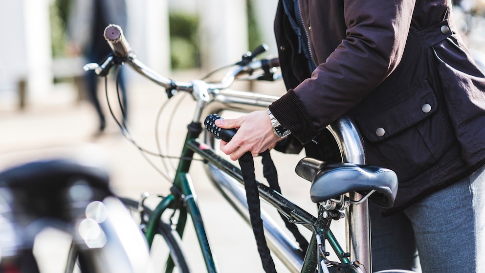 Mann schließt Fahrrad mit Fahrradschloss an.