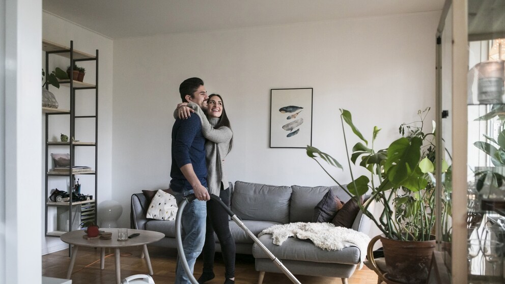 Paar im Wohnzimmer, Mann hält Staubsauger und Frau in der Hand