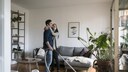 Paar im Wohnzimmer, Mann hält Staubsauger und Frau in der Hand
