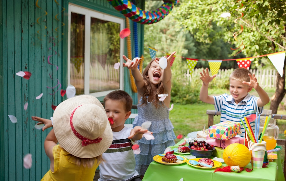 Kinder werfen Konfetti im Garten bei der Geburtstagsparty in die Luft