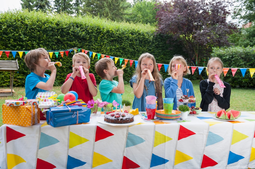 Sechs Kinder stehen an dem Geburtstagstisch und pusten in Luftschlangen