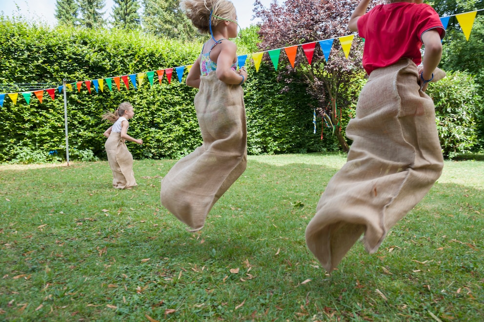 Drei Kinder beim Sackhüpfen im Garten