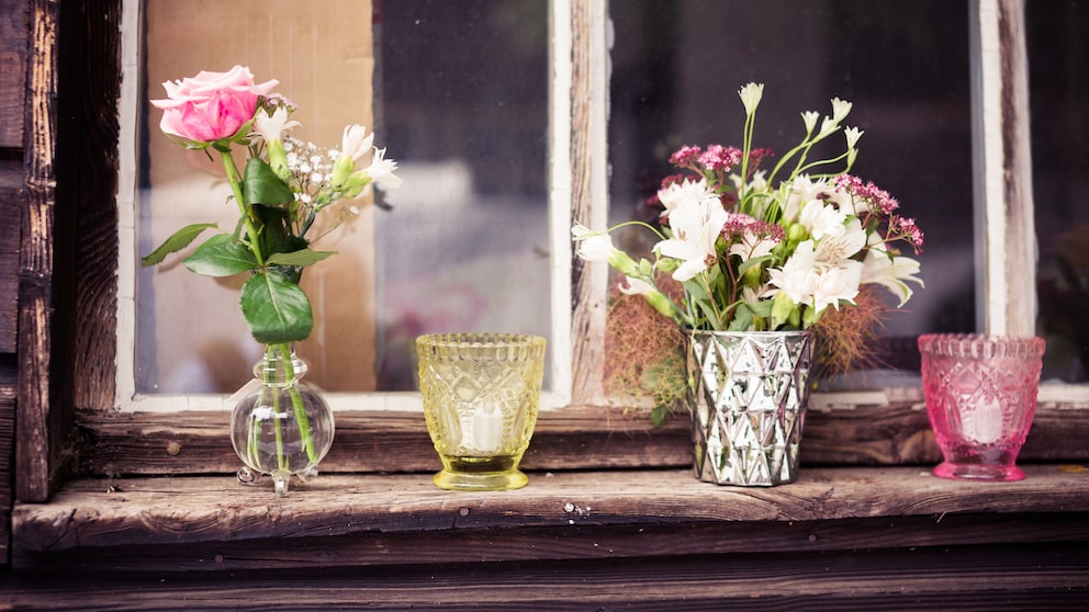Auf einem Fensterbrett stehen Blumenvasen und Kerzen