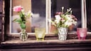 Auf einem Fensterbrett stehen Blumenvasen und Kerzen