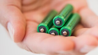 In einer Hand liegen vier grüne Batterien.