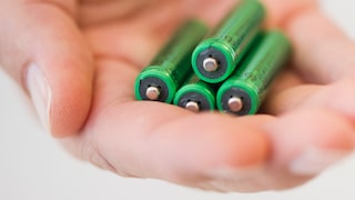 In einer Hand liegen vier grüne Batterien.