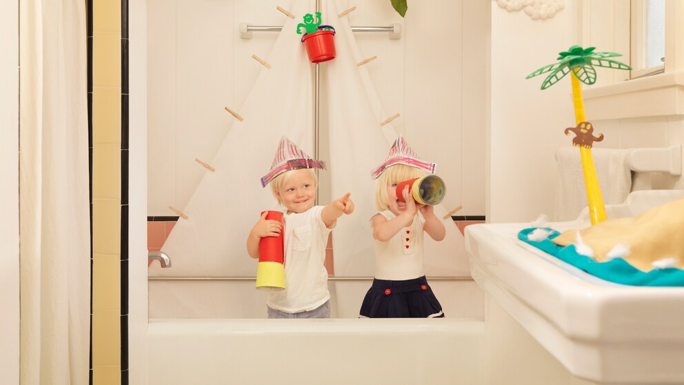 Zwei Kinder sitzen in einer Badewanne und spielen Bootfahren.