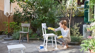 Gartenmöbel: Frau streicht alte Gartenstühle weiß