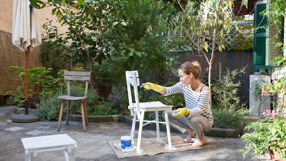Gartenmöbel: Frau streicht alte Gartenstühle weiß