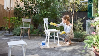 Gartenmöbel: Frau streicht alte Gartenstühle weiß
