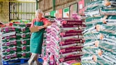 Ein Mitarbeiter steht vor mehreren Paletten mit Blumenerdesäcken. In der Hand hält er eine Lade. Darauf macht er Notizen.