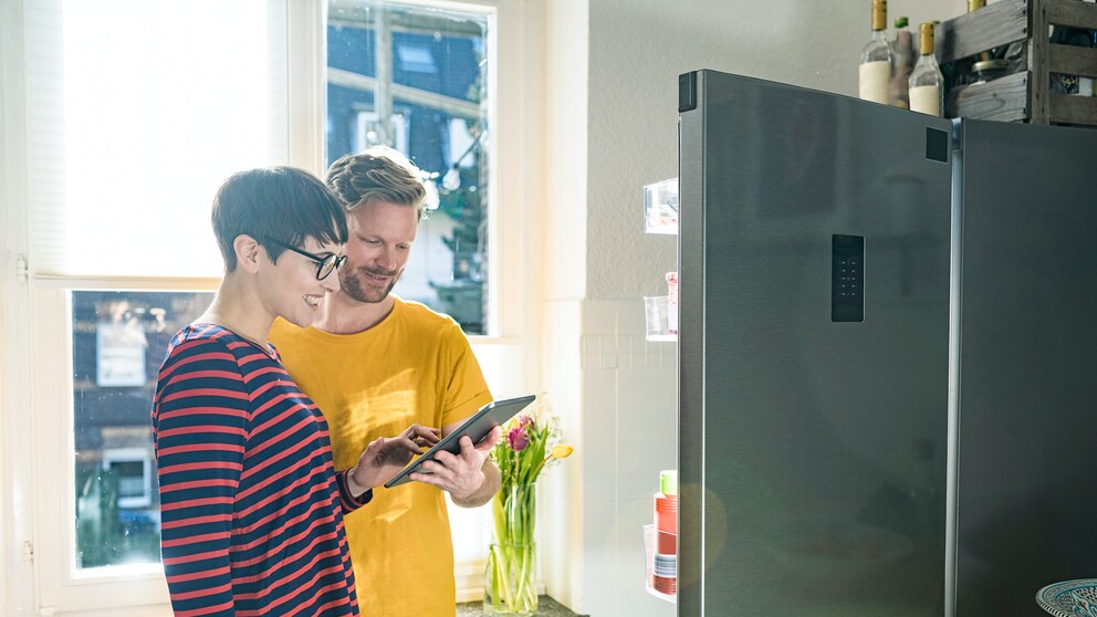 Ein Pärchen steht vor einem modernen Kühlschrank