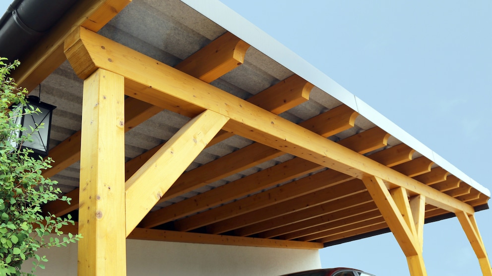 Ein Auto steht unter einem Carport aus Holz.