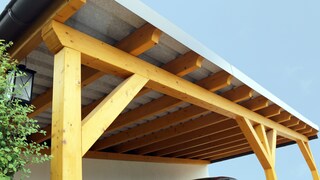 Ein Auto steht unter einem Carport aus Holz.