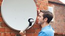 Ein Mann montiert eine Satellitenschüssel an der Hauswand