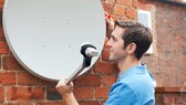Ein Mann montiert eine Satellitenschüssel an der Hauswand