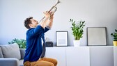 Mann sitzt auf einer Couch und spielt Trompete