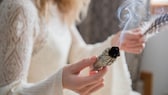 Eine Frau hält ein Räuchermaterial in der rechten Hand und eine Feder in der linken Hand