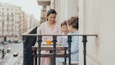 Frau frühstückt mit Kindern auf dem Balkon