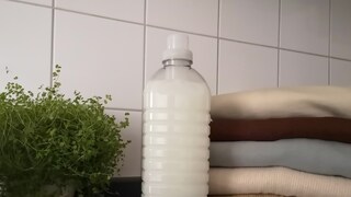 Waschmittel steht vor Kleiderstapel und Pflanze
