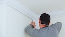 Mann bringt Stuckleisten an der Wand an