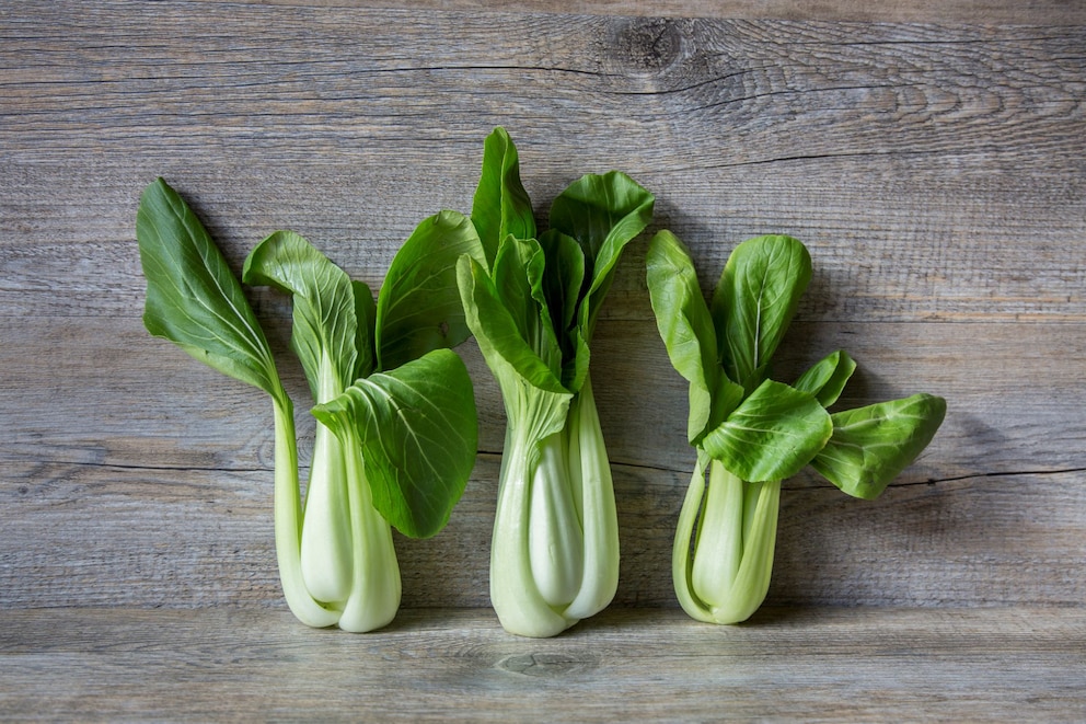 3 Pak Choi liegen nebeneinander auf einem hölzernen Untergrund