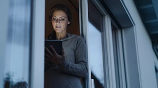 Frau steht in der Balkontür mit einem Tablet in der Hand