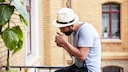 Mann mit Hut raucht auf dem Balkon