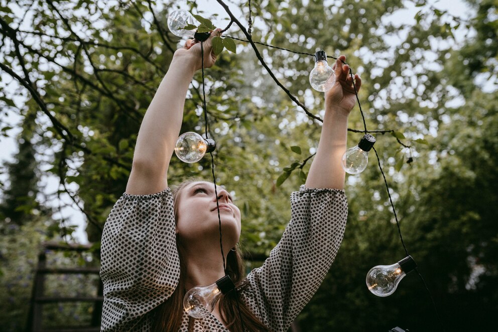 Eine junge Frau hängt eine Lichterkette in einem Baum auf