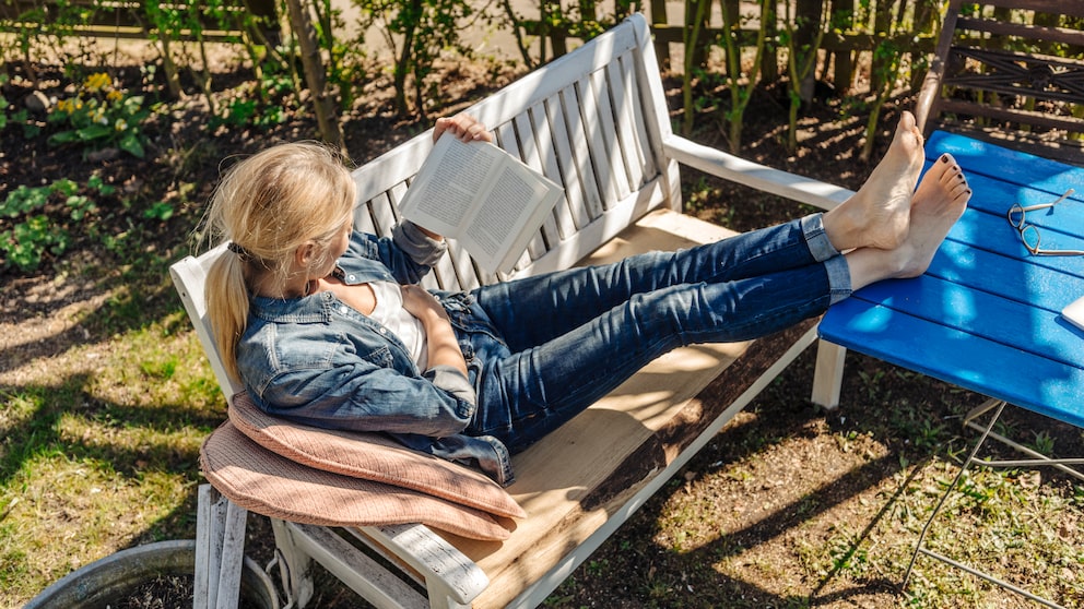 Gartenmöbel Sicherheit: Eine Frau liegt auf einer Gartenbank und liest ein Buch