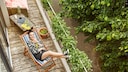 : Junge Frau, die sich auf ihrem schmalen Balkon in einer Sonnenliege entspannt