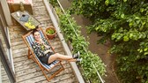 : Junge Frau, die sich auf ihrem schmalen Balkon in einer Sonnenliege entspannt