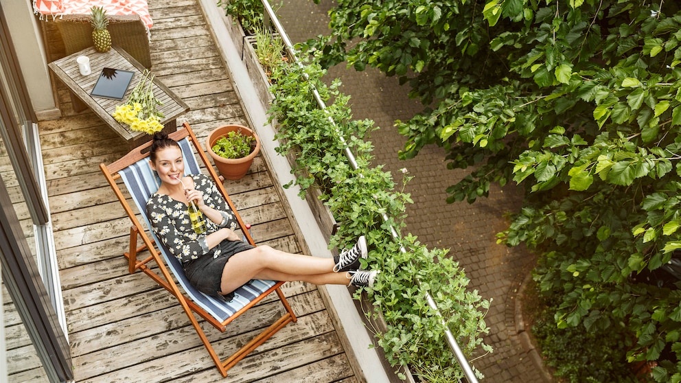 : Junge Frau, die sich auf ihrem schmalen Balkon in einer Sonnenliege entspannt