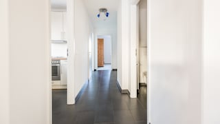 Langer, schmaler Flur mit weißen Wänden und dunklem Boden