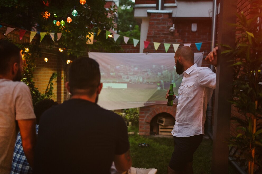 Drei Fußballfans verfolgen ein Spiel via Leinwand und Beamer im Garten