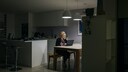 Frau, die in einer dunklen, innenliegenden K&uuml;che ohne Fenster, sitzt und am Laptop arbeitet