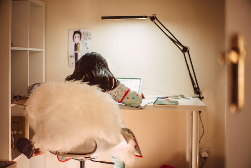 Child sitting on an adjustable swivel chair at a desk doing homework