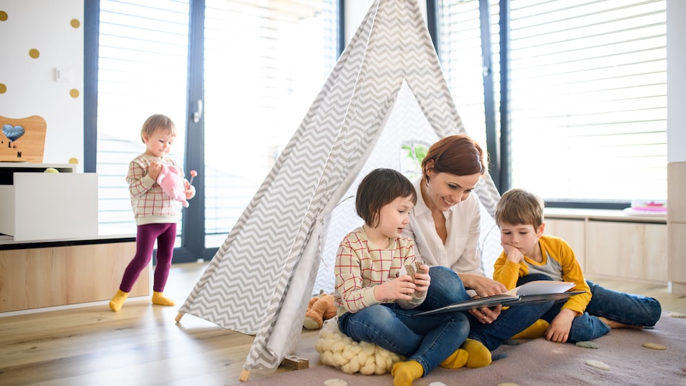 Mutter, die mit ihren Kindern im gemütlichen Tipi ein Buch liest