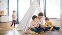 Mutter, die mit ihren Kindern im gemütlichen Tipi ein Buch liest