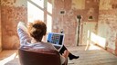 Ein Mensch sitzt mit Laptop vor einer abgerissenen Wand