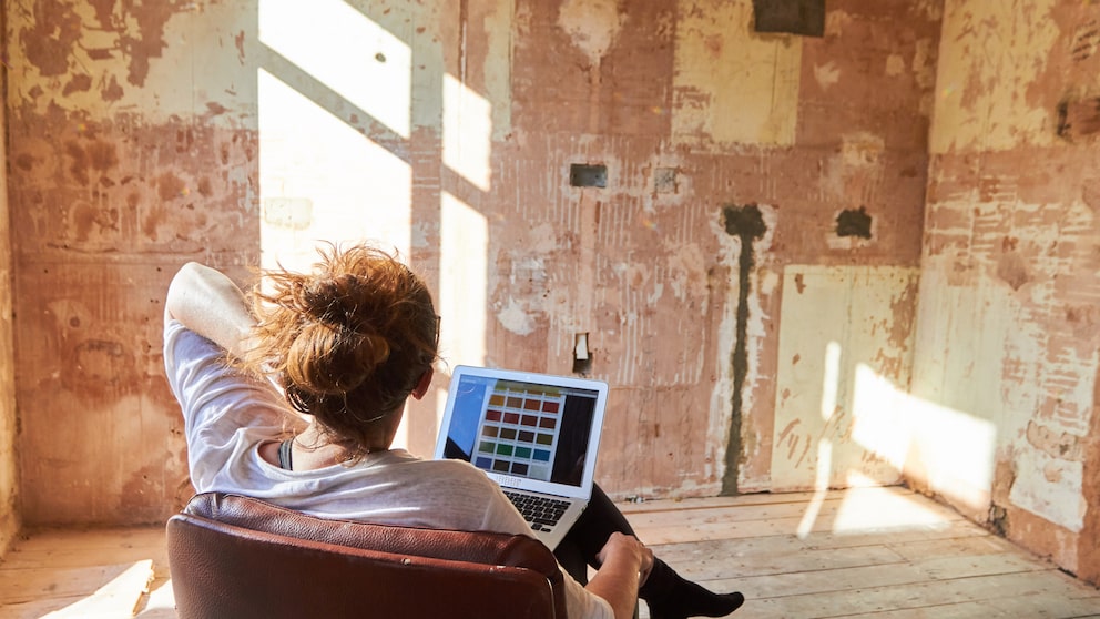 Ein Mensch sitzt mit Laptop vor einer abgerissenen Wand