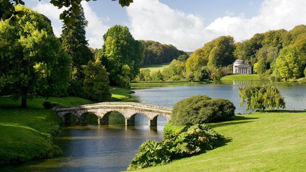 Gartenkunst: Blick auf Fluss mit steinerner Brücke in einem englischen Landschaftsgarten